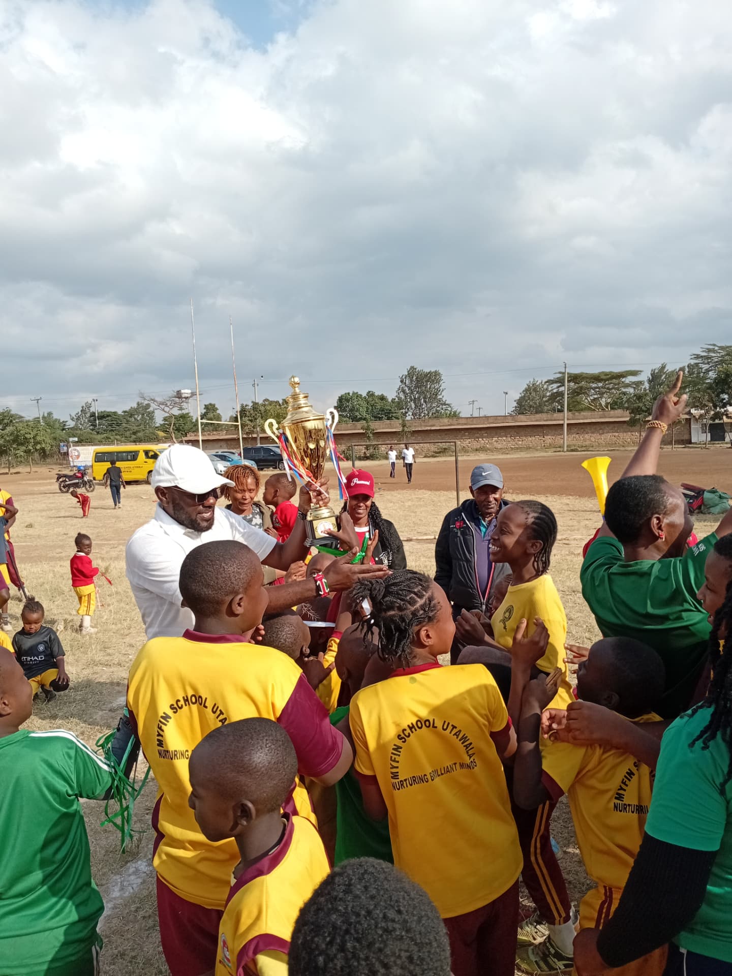 Myfin School team huddled around a champions trophy with coaches and supporters