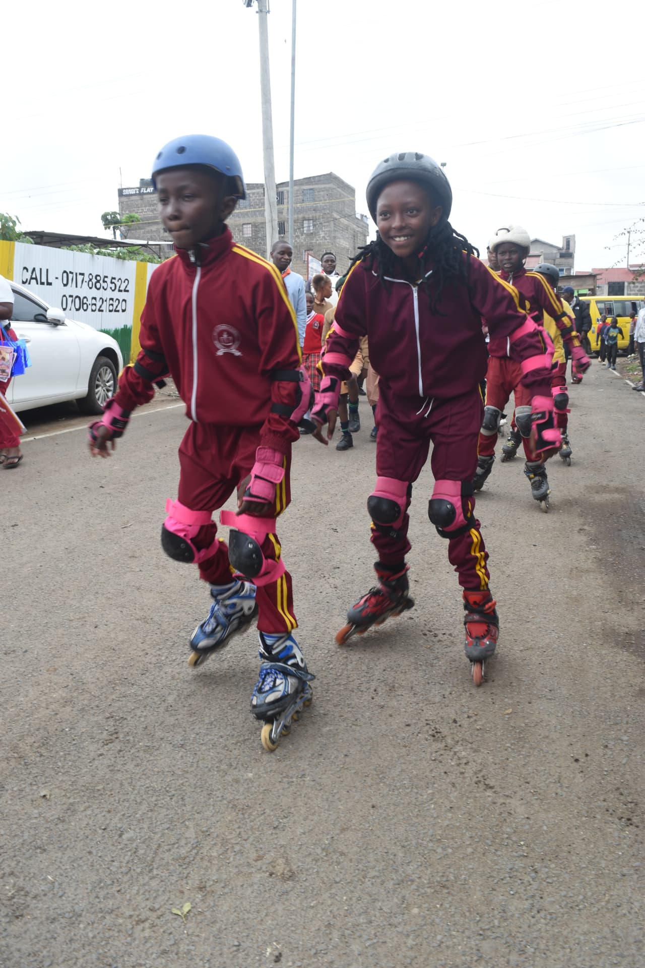 Myfin School skaters in maroon tracksuits, helmets and pads rolling along the road