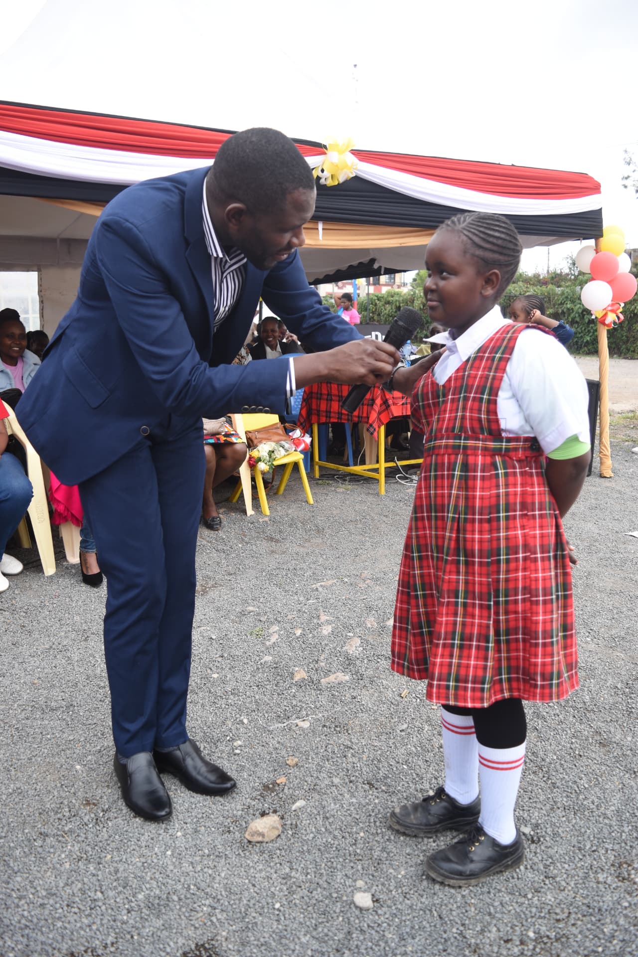 Myfin School learner in red tartan uniform answering questions on a microphone