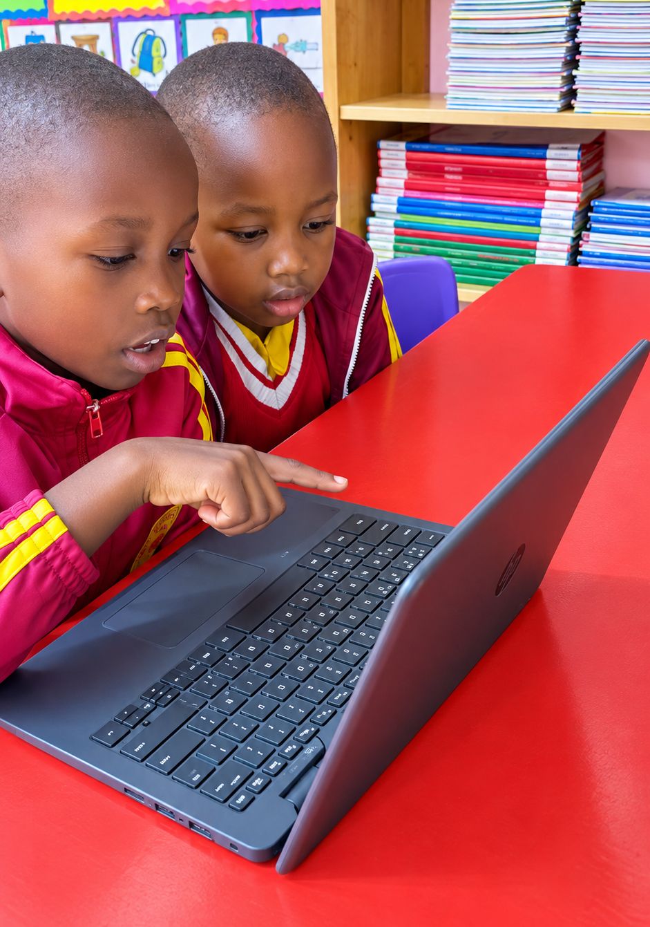 Myfin School learners in red and yellow uniforms exploring a laptop together in an AI lesson